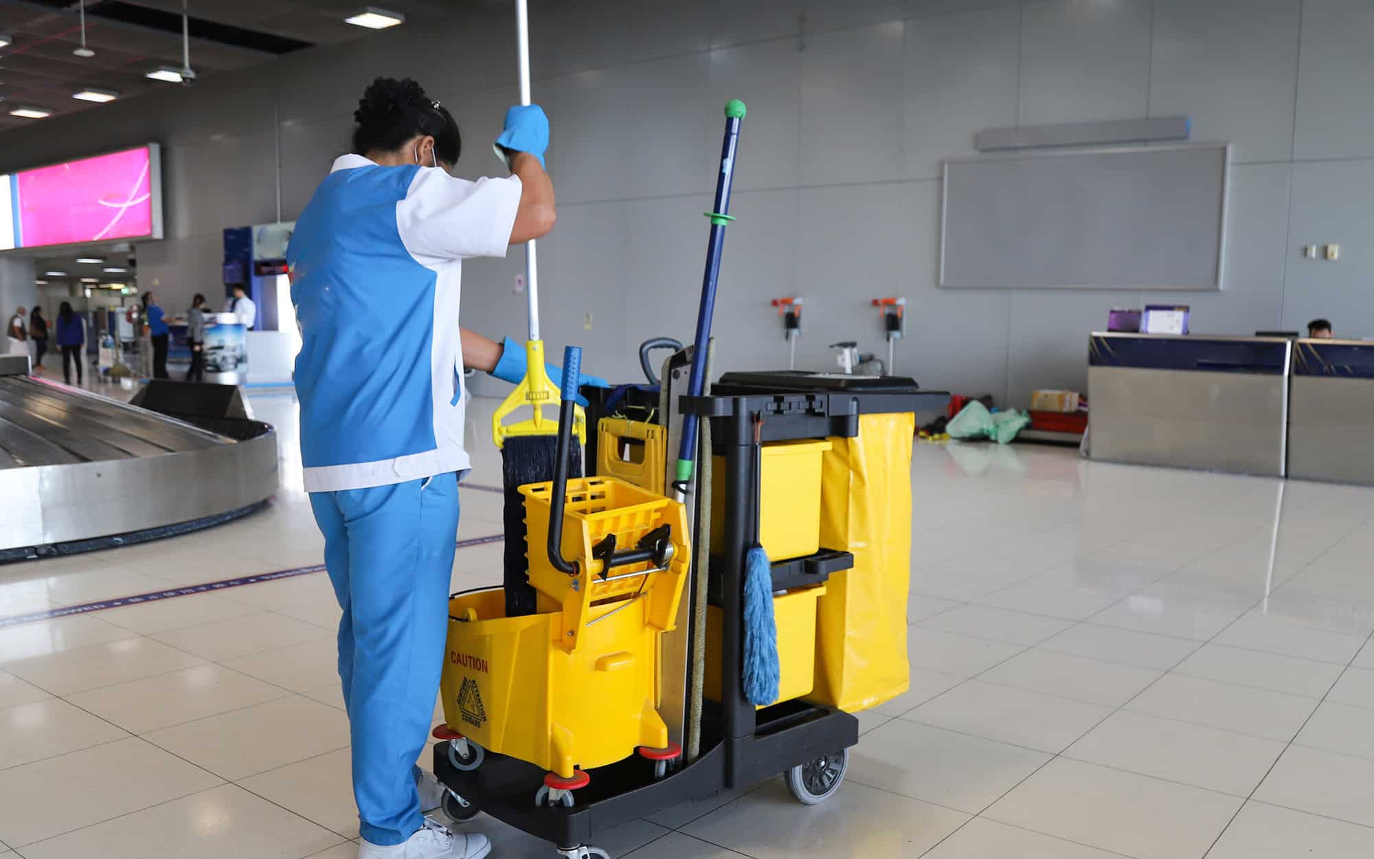 Side View, Woman In Airport Cleaning The Floor While Standing At Mop Cart